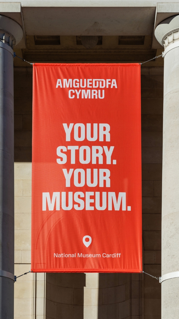 A photo of a red banner hanging outside the National Museum Cardiff. The banner reads 'Your story. Your museum'.