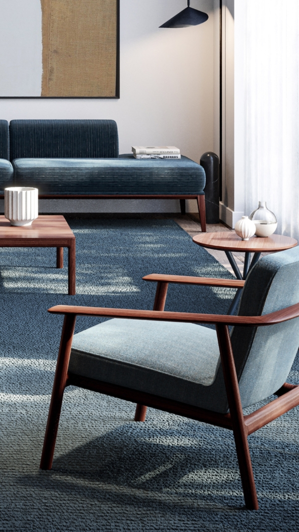 A room set with the Kato lounge chair by Lyndon in the foreground. The chair has a walnut frame and grey blue upholstery.