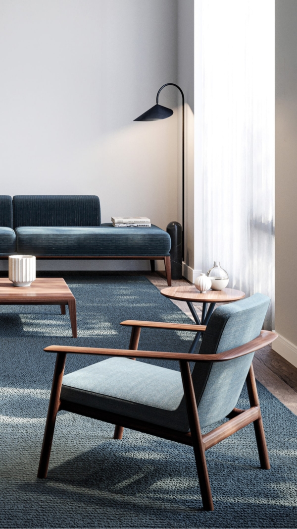 A room set with the Kato lounge chair by Lyndon in the foreground. The chair has a walnut frame and grey blue upholstery.
