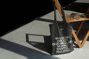 A promotional black tote bag for the 'Art of the Selfie exhibition'. A list of artists included in the exhibition are printed on the bag in bold white text.